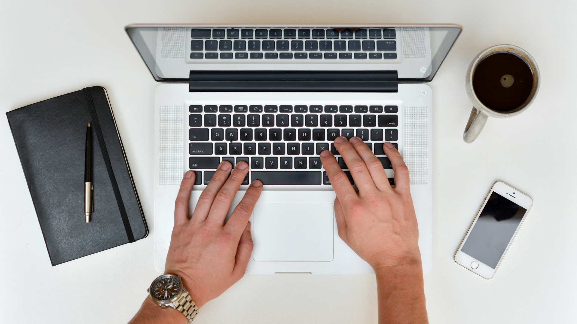 Aerial view of a macbook laptop with a notepad, coffe and phone next to it